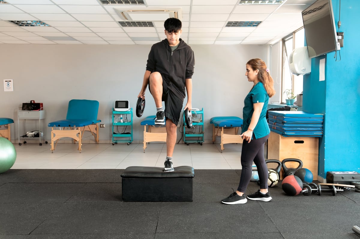 Physiotherapist supervising young patient doing box step exercise